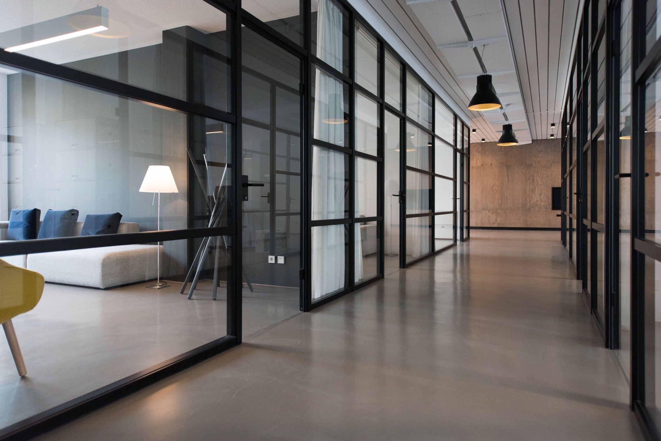 A picture of a hallway in a shared office space building. You can see office furniture behind glass walls.